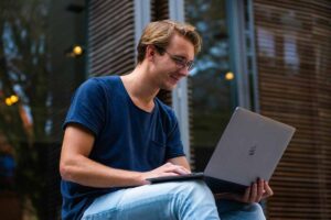 ragazzo seduto che sorride mentre guarda il computer che tiene sulle gambe